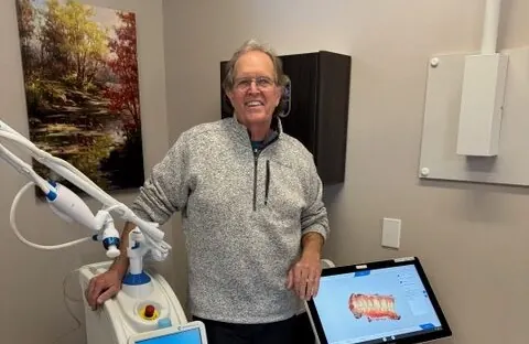 Dr. Dean beside the Primescan scanner, its screen showing a 3D scan of a patient's teeth.